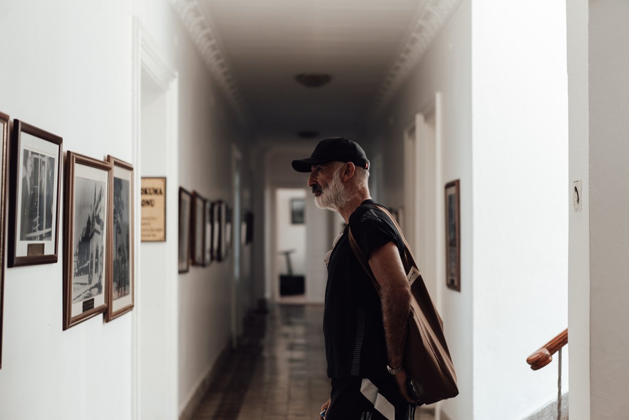 Serious elderly ethnic man looking at pictures hanging on wall in hall